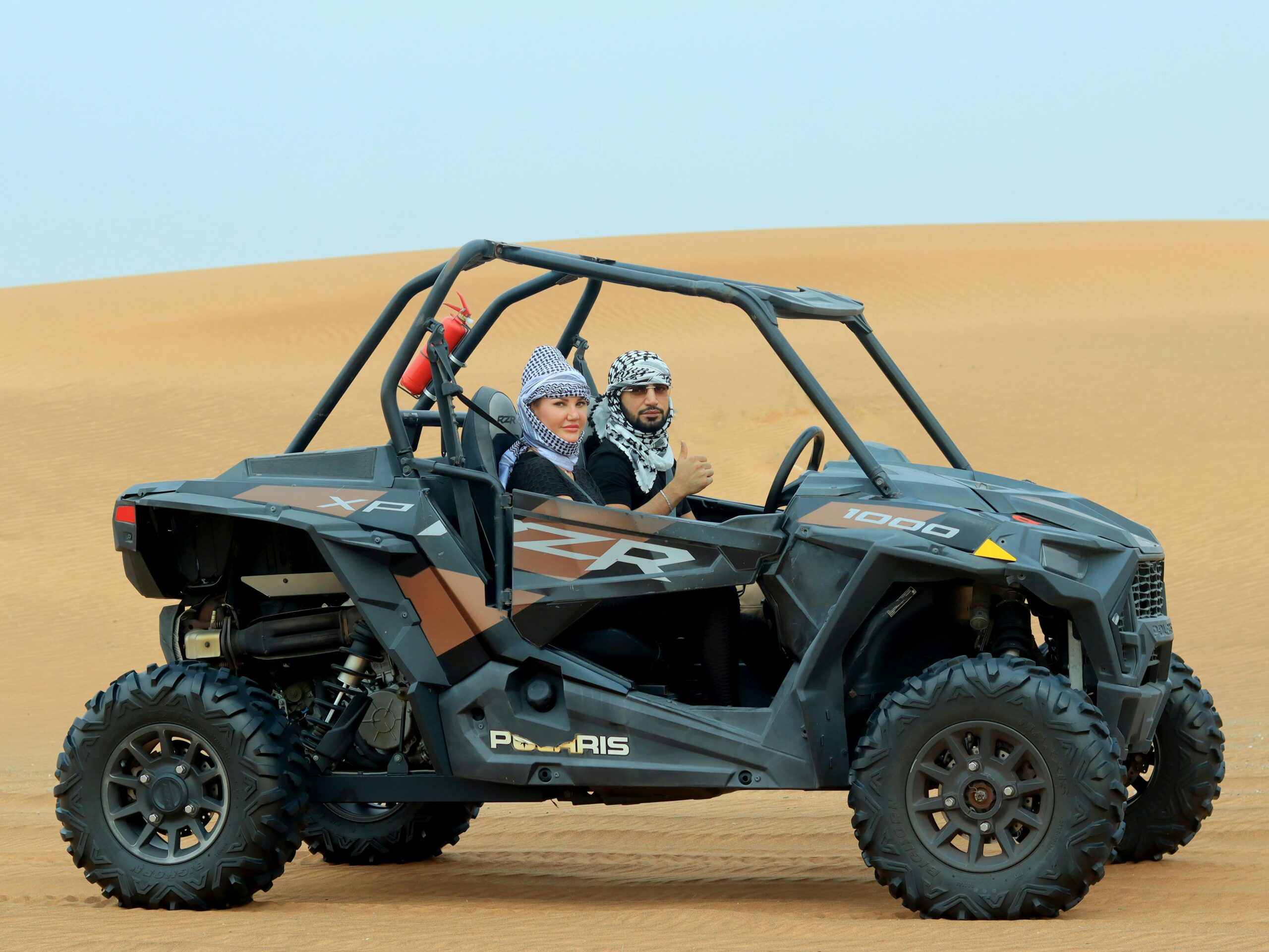 A couple driving a buggy through the sandy desert in Dubai, United Arab Emirates.