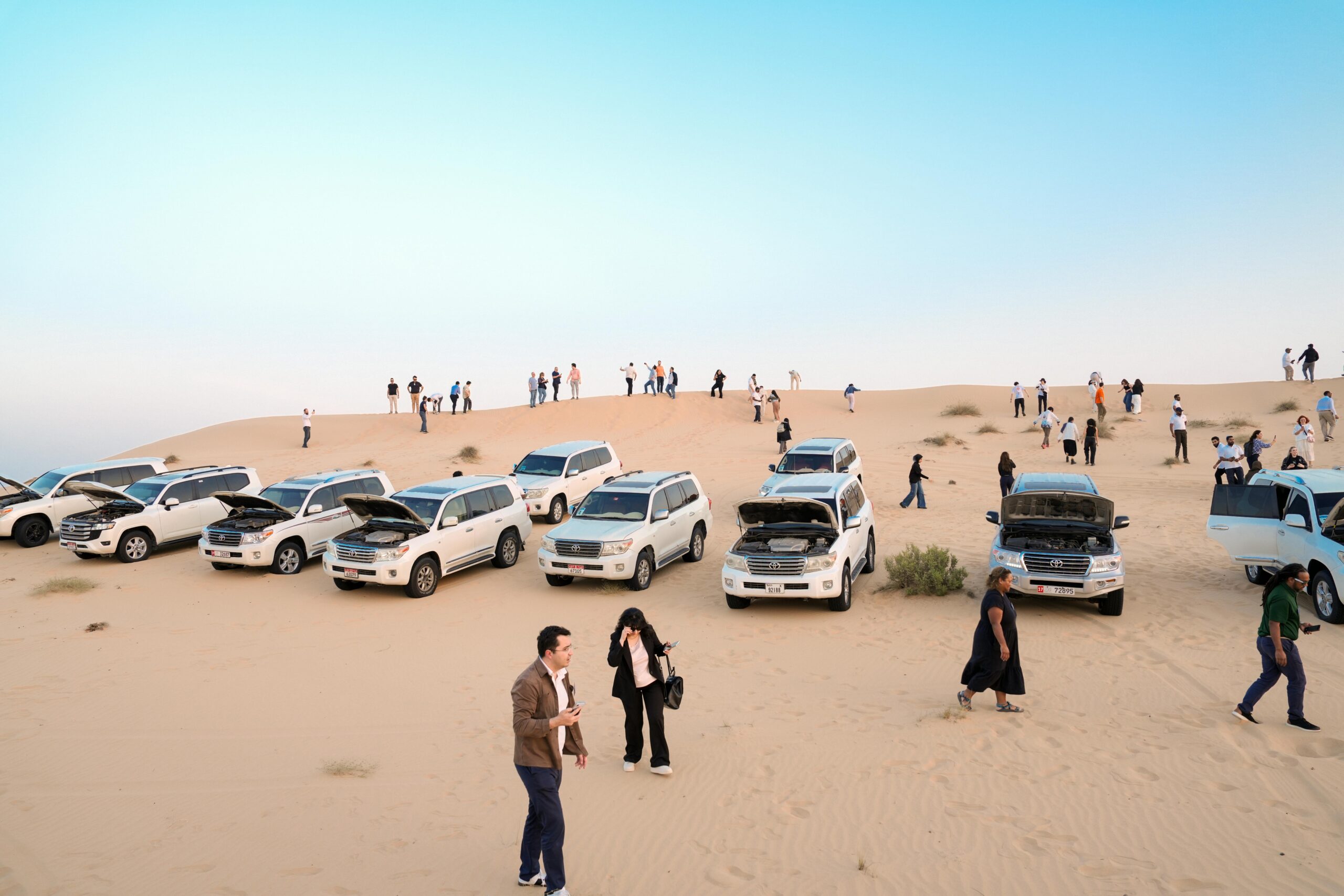 A group of tourists and SUVs on a sandy desert dune during daytime.